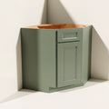 Angled view of a green Belmont beveled Shaker diagonal corner sink base cabinet with 1 door and 1 false drawer.