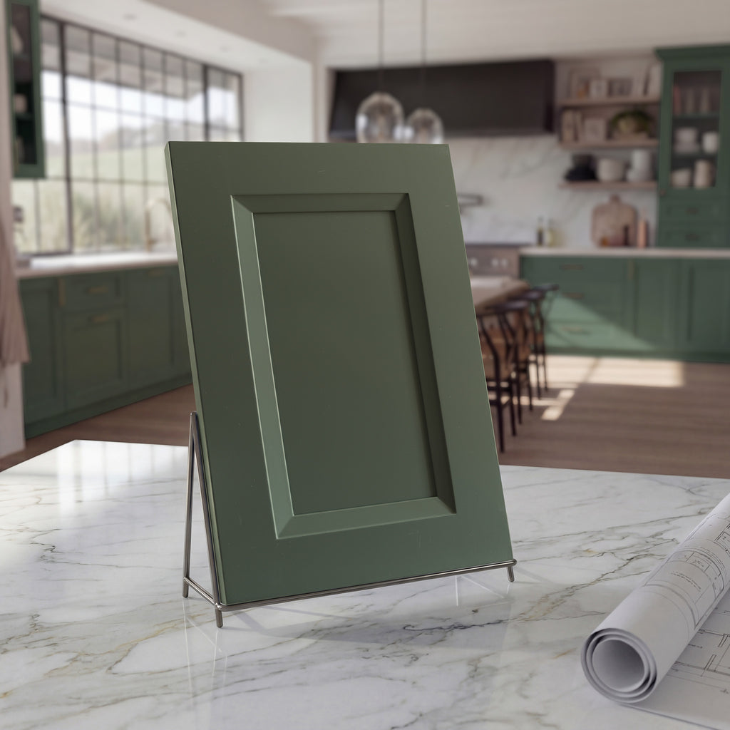Angled Belmont green beveled shaker cabinet door sample on a white stone countertop against a contemporary kitchen backdrop.