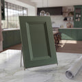Angled Belmont green beveled shaker cabinet door sample on a white stone countertop against a contemporary kitchen backdrop.