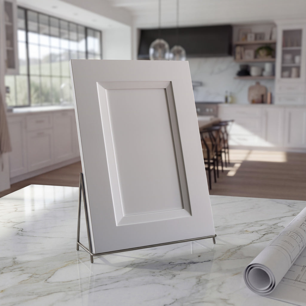 Angled Belmont white beveled shaker cabinet door sample on a white stone countertop against a contemporary kitchen backdrop.