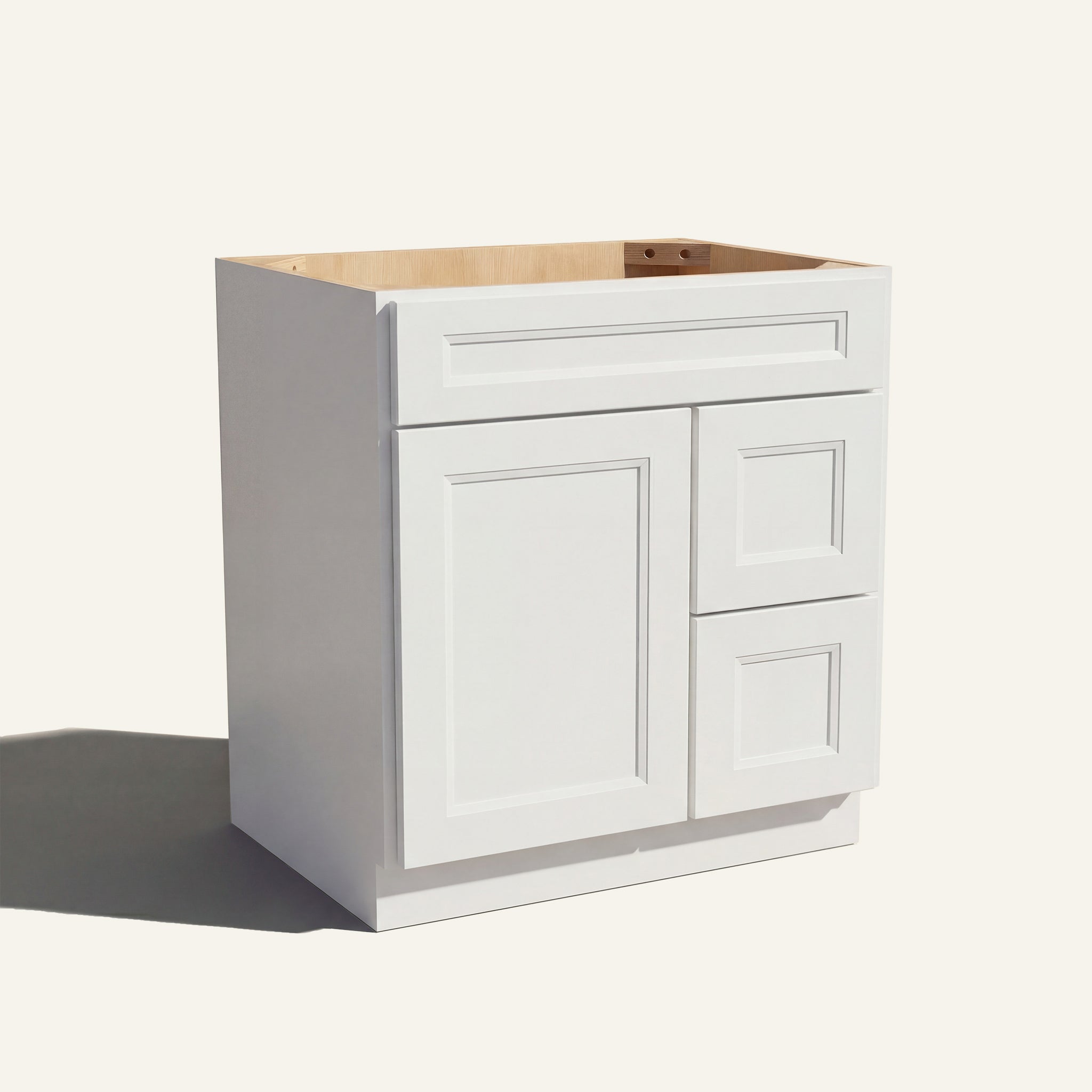 Angled view of a white Belmont beveled shaker single sink vanity with a left-side door and two right-side drawers.