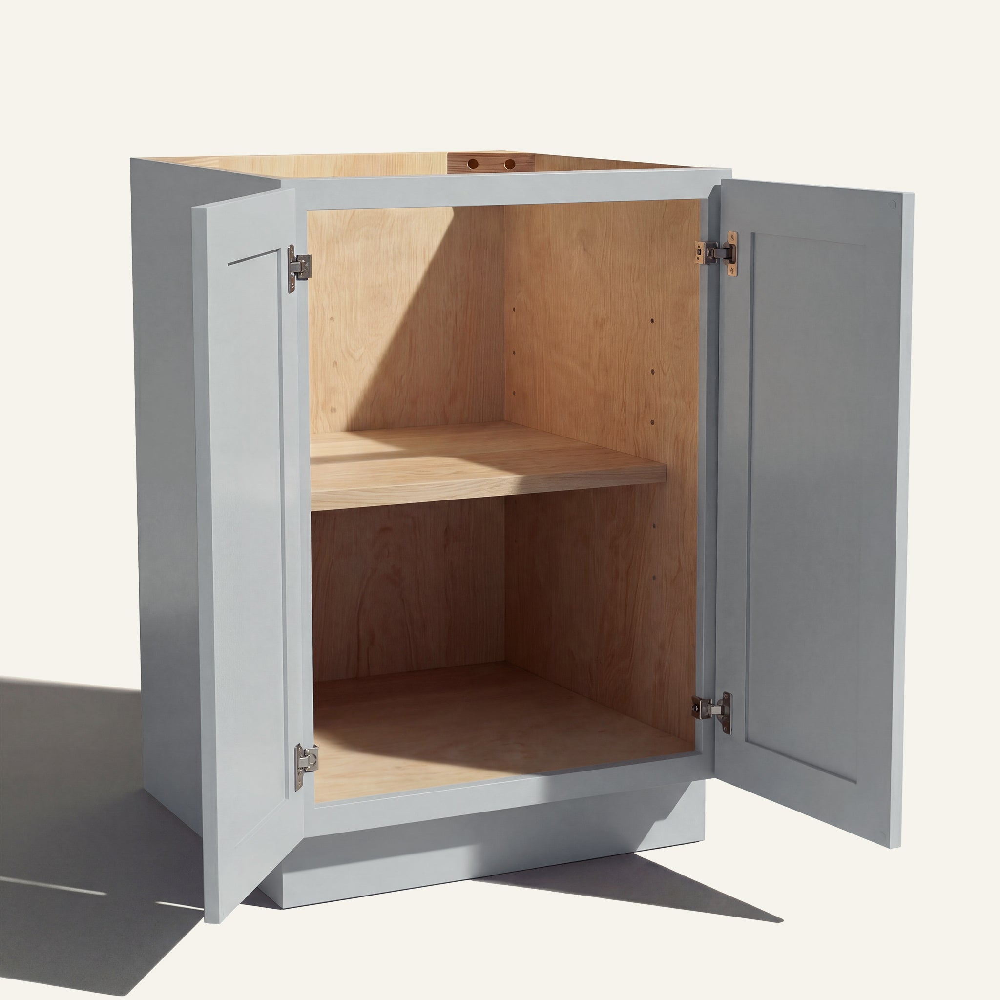 Angled view of a light gray Seaport Shaker base cabinet with 2 full height doors open showing wood interior and shelf.