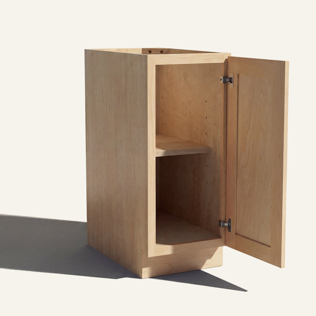Angled view of a natural Seaport Shaker base cabinet with 1 door open showing wood interior and shelf.
