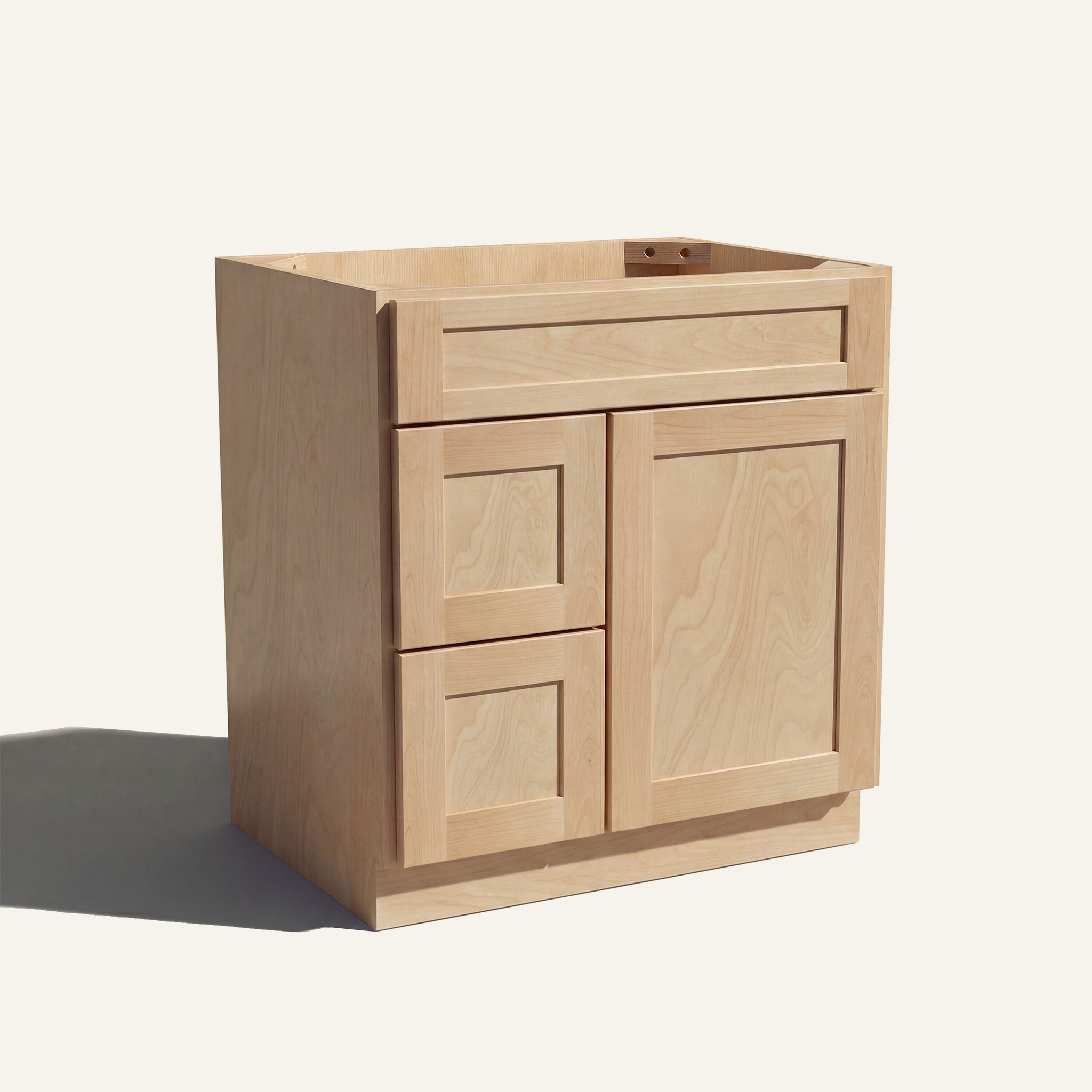 Angled view of a natural Seaport shaker single sink vanity with a right-side door and two left-side drawers.